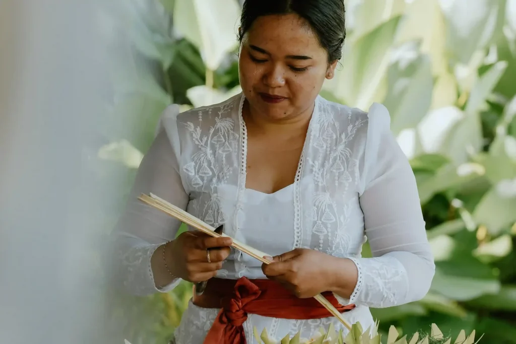 A Balinese woman folding palm leaf into a canang sari offering