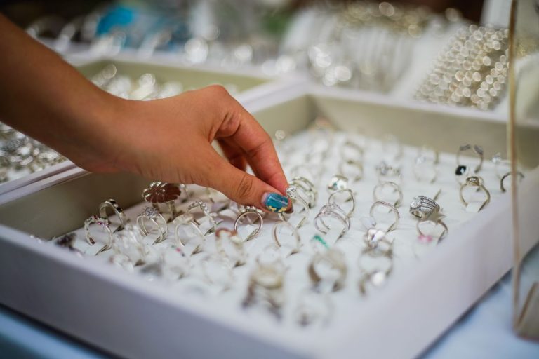 A hand lifting a silver ring from a tray of rings and bracelets in a jewellery shop
