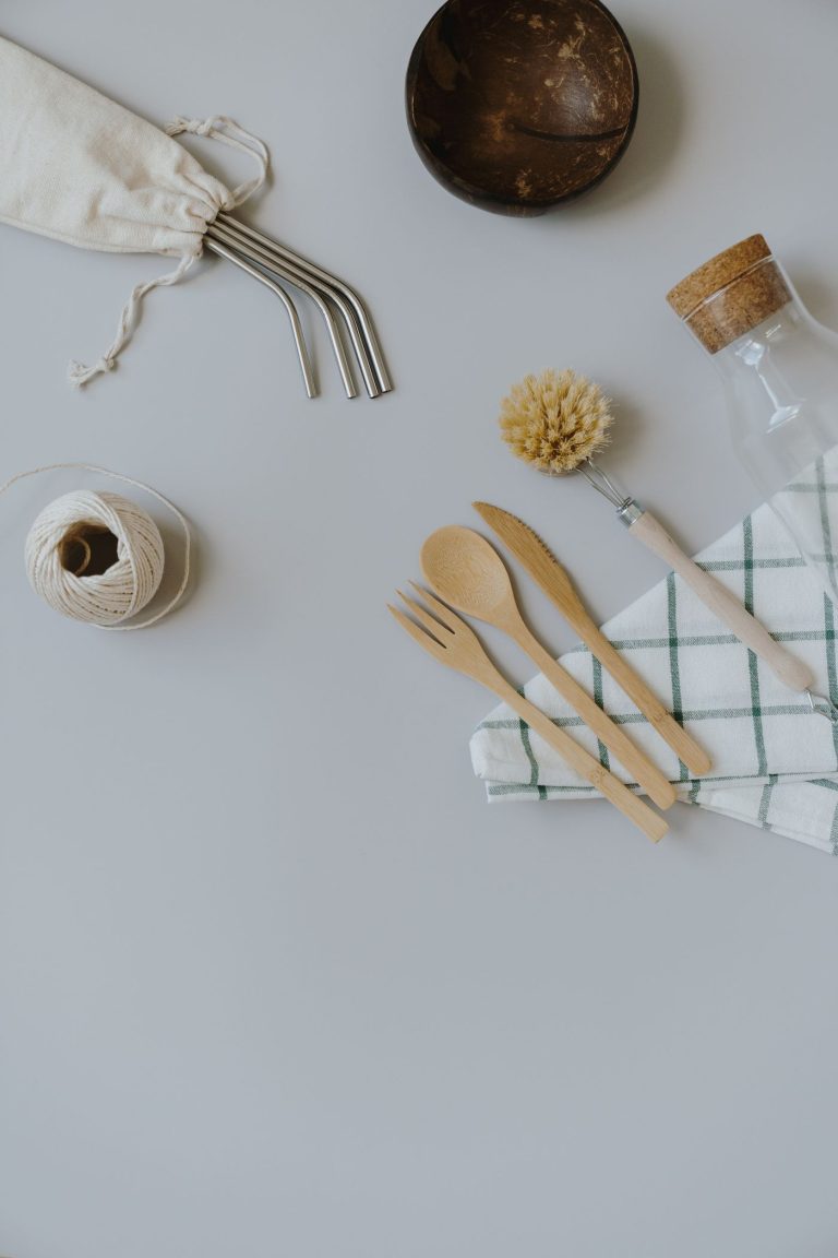 A flat lay of bamboo cutlery, a reusable cup and a mesh bag on a pale surface