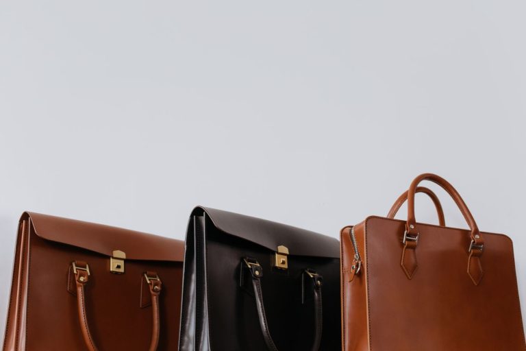 Three structured leather handbags in tan, black and brown on a pale background