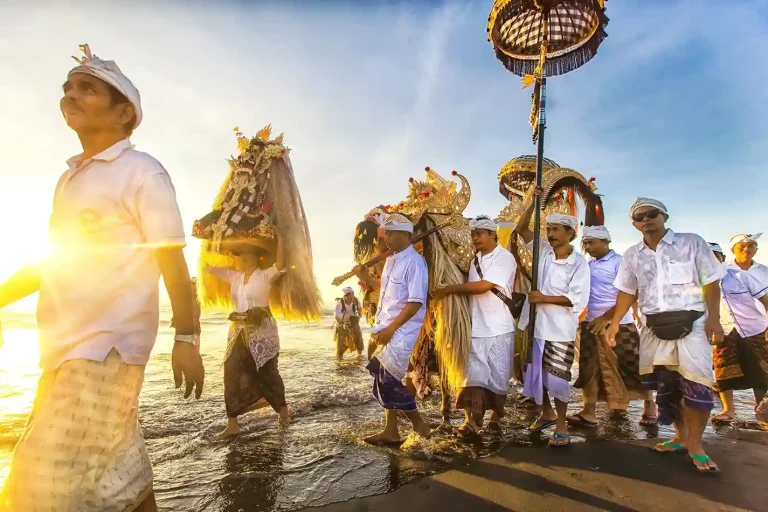Balinese devotees in white carrying ceremonial umbrellas along the shore during Melasti