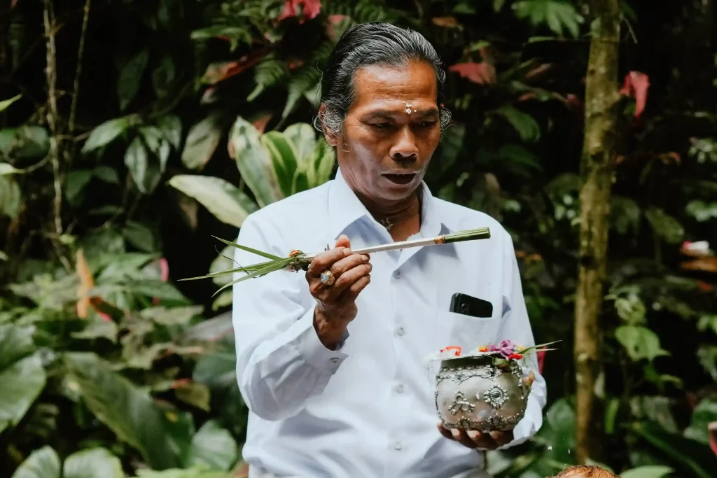 A Balinese pemangku holding a ritual vessel during a melukat purification