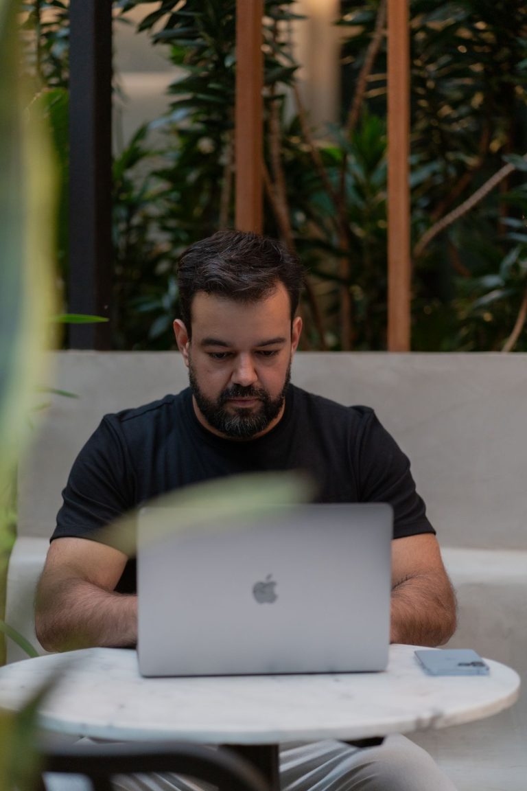 A man working on a laptop at a table surrounded by tropical planting