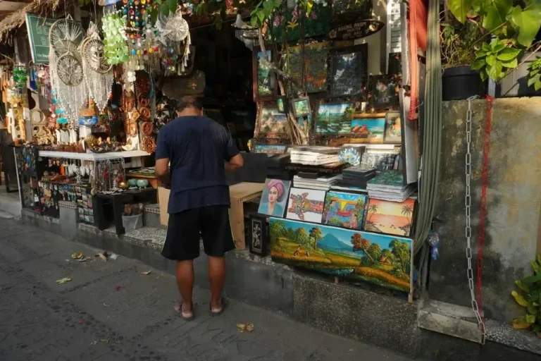 A visitor looking over paintings and crafts at an Ubud art market stall