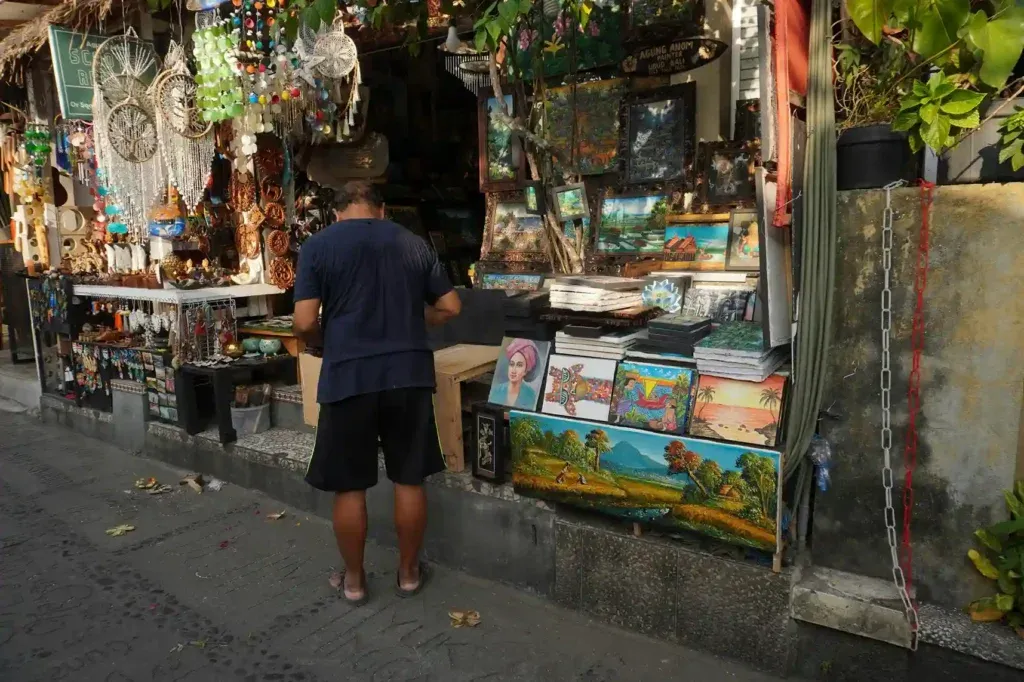A visitor looking over paintings and crafts at an Ubud art market stall